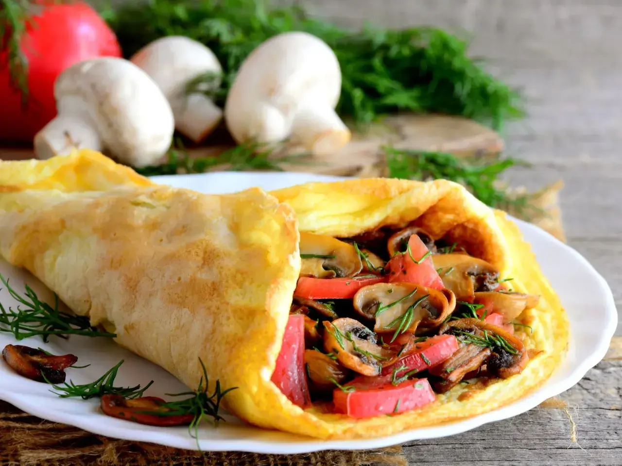 Puszysty omlet z pieczarkami i pomidorami, udekorowany koperkiem.