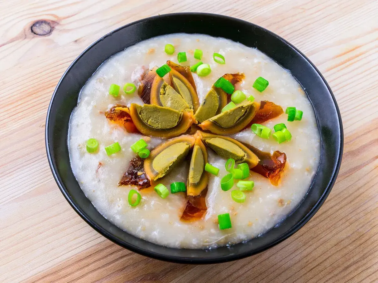 Miseczka z congee, ozdobiona połówkami jajka stuletniego, posypana szczypiorkiem i skropiona olejem chili.