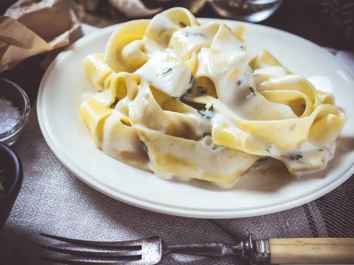 Makaron tagliatelle w kremowym sosie serowym z ziołami na białym talerzu.