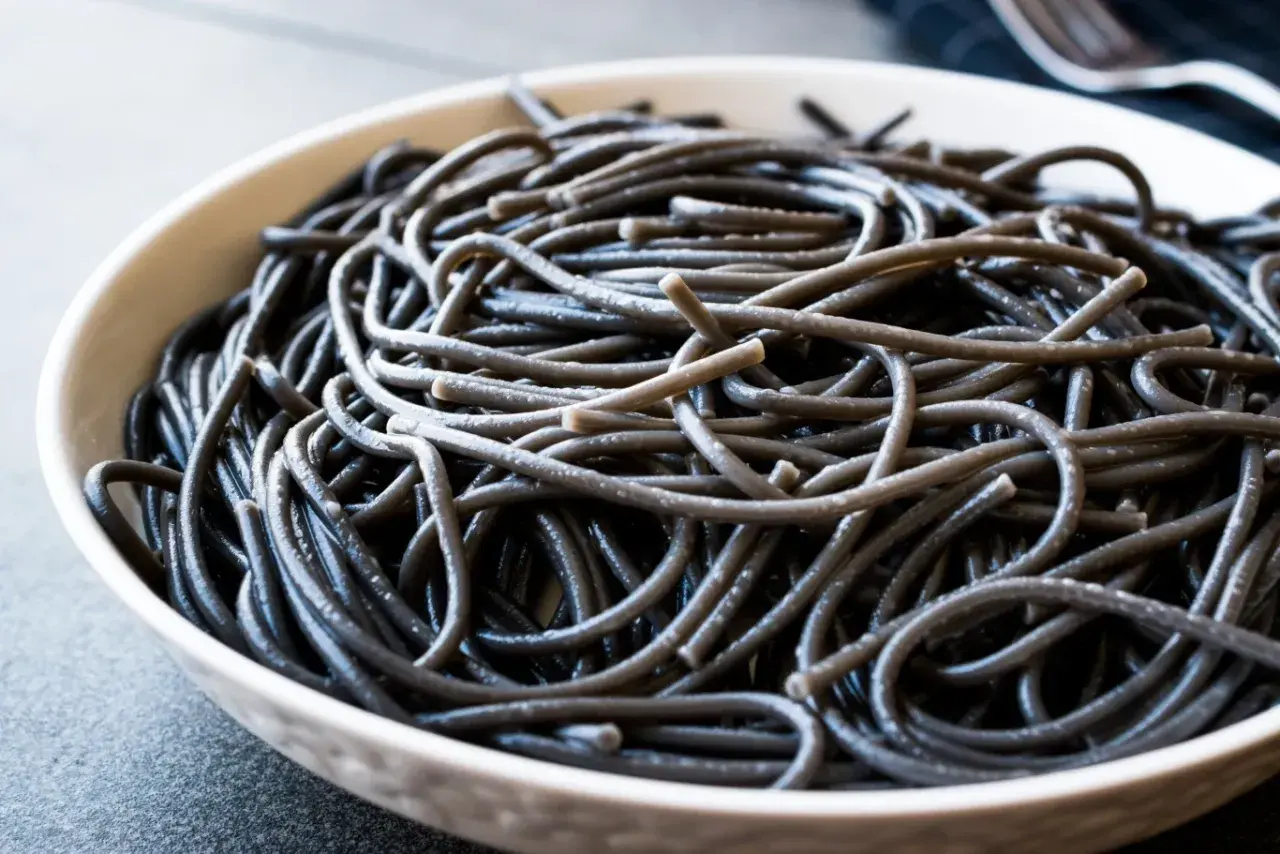 Czarny makaron spaghetti w białej misce, zbliżenie.
