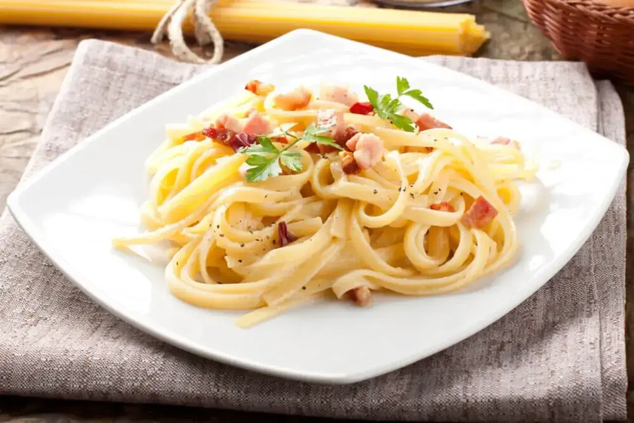 Talerz spaghetti carbonara z boczkiem i natką pietruszki, na lnianej serwetce.