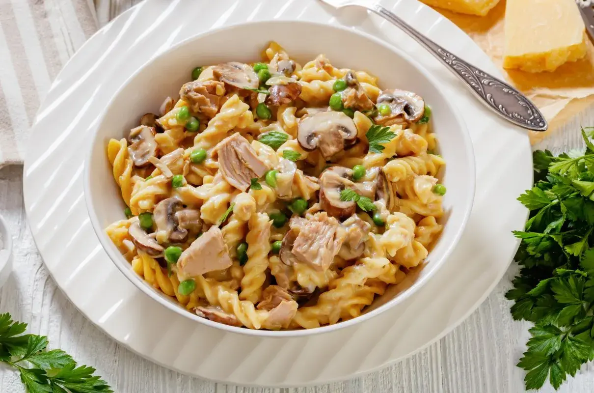 Makaron fusilli z tuńczykiem, groszkiem i pieczarkami w kremowym sosie, udekorowany natką pietruszki.