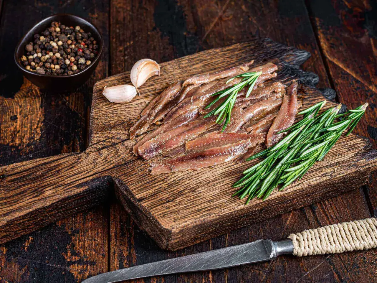 Filety anchois z rozmarynem i czosnkiem na drewnianej desce.