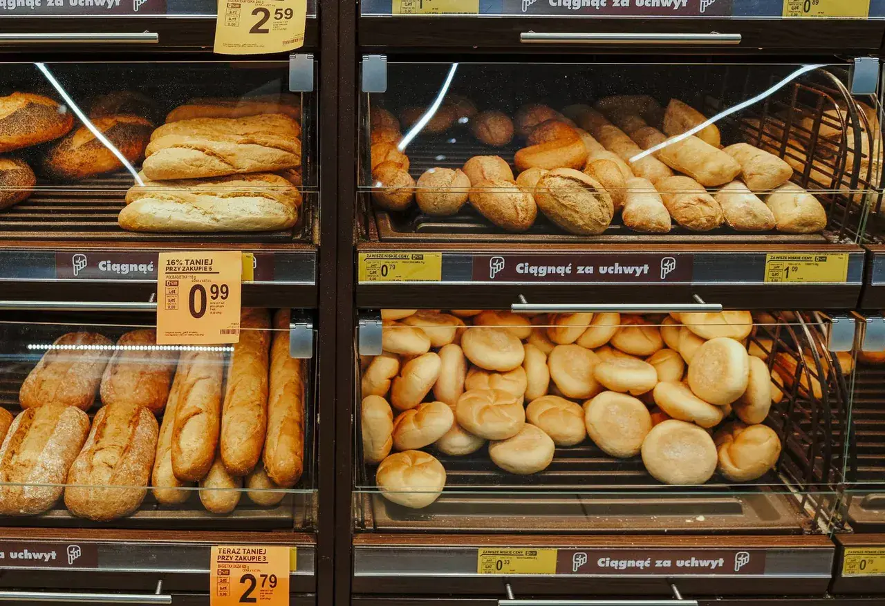 Różne rodzaje pieczywa, w tym bochenki i bułki, wystawione na sprzedaż w sklepie.