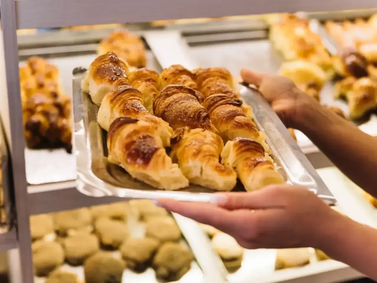 Taca z croissantami, którą trzymają ręce, na tle innych wypieków.