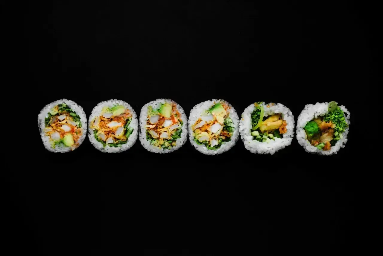 Sześć grubych rolek sushi futomaki z widocznym nadzieniem na czarnym tle.