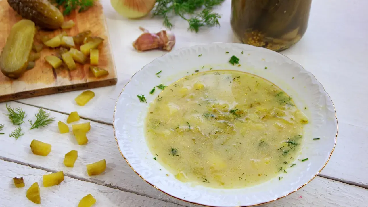 Talerz zupy ogórkowej, obok deska z ogórkami, koperek i cebula.