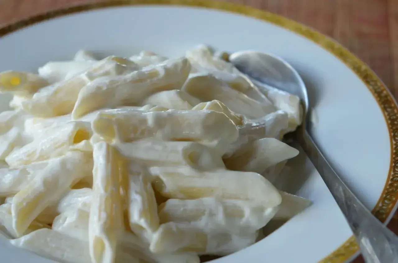 Makaron penne w kremowym sosie z twarogu na talerzu ze srebrną łyżką.