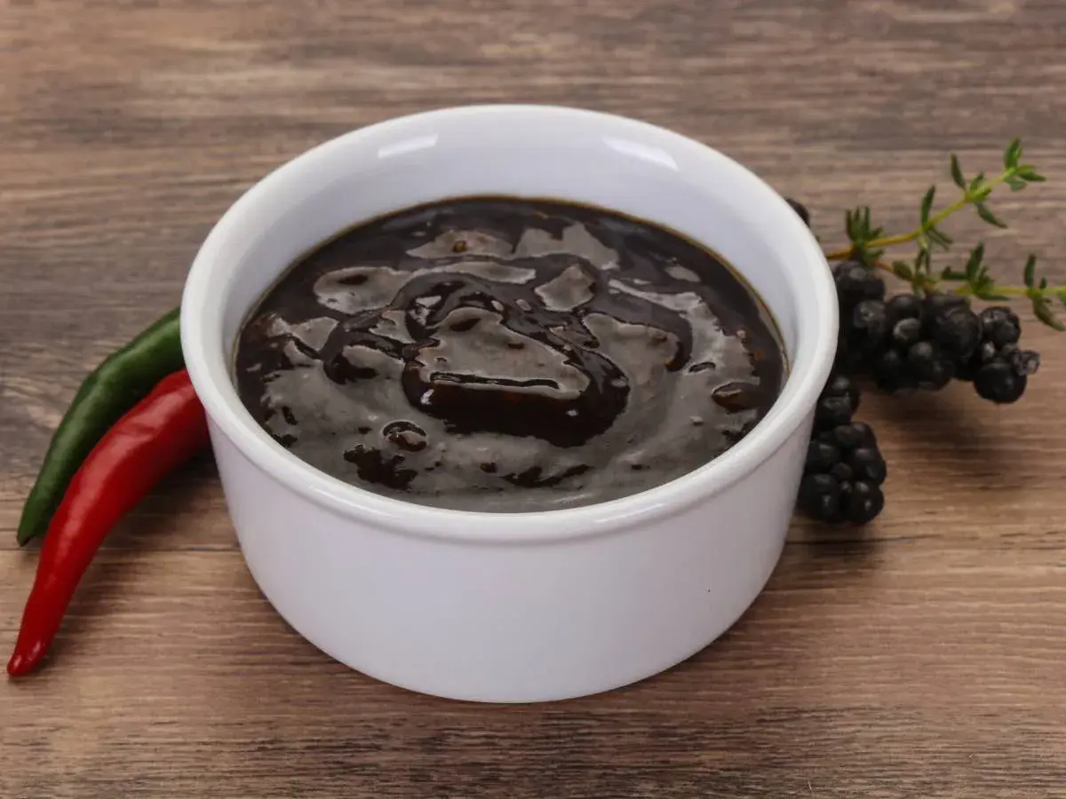 Miseczka z ciemnym sosem pieprzowym, obok papryczki chili i jeżyn.