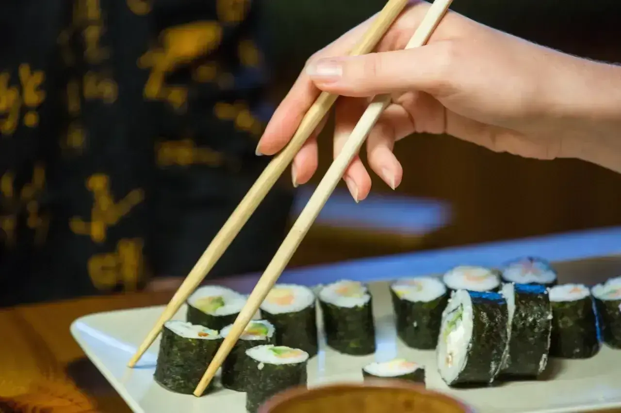 Dłoń z pałeczkami sięga po rolkę sushi. Smaczne i zdrowe, ale warto pamiętać o sushi kcal.