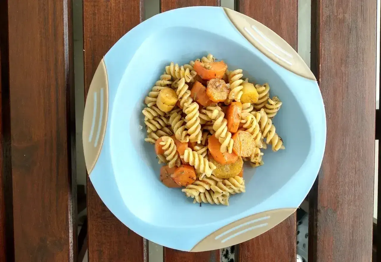 Makaron fusilli z marchewką i ziemniakami na niebieskim talerzyku.