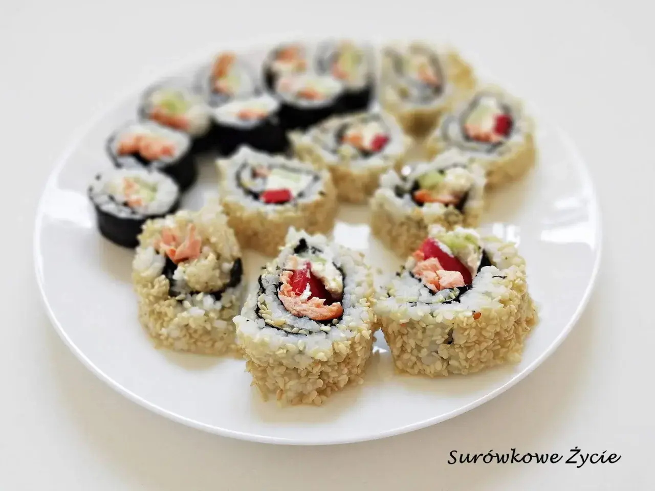Talerz z rolkami sushi uramaki z ryżem na zewnątrz, posypanymi sezamem, z łososiem i warzywami.