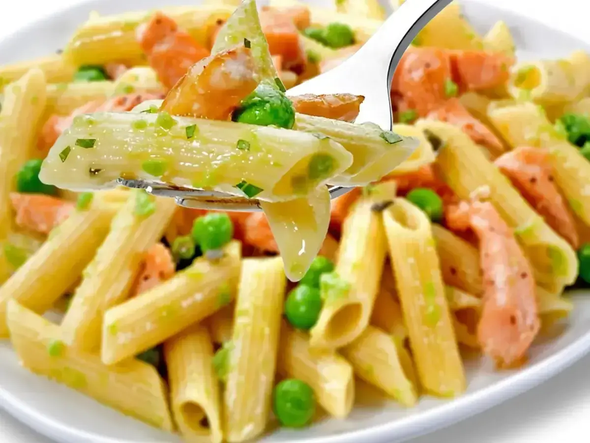 Makaron penne z łososiem i groszkiem w kremowym sosie na widelcu.