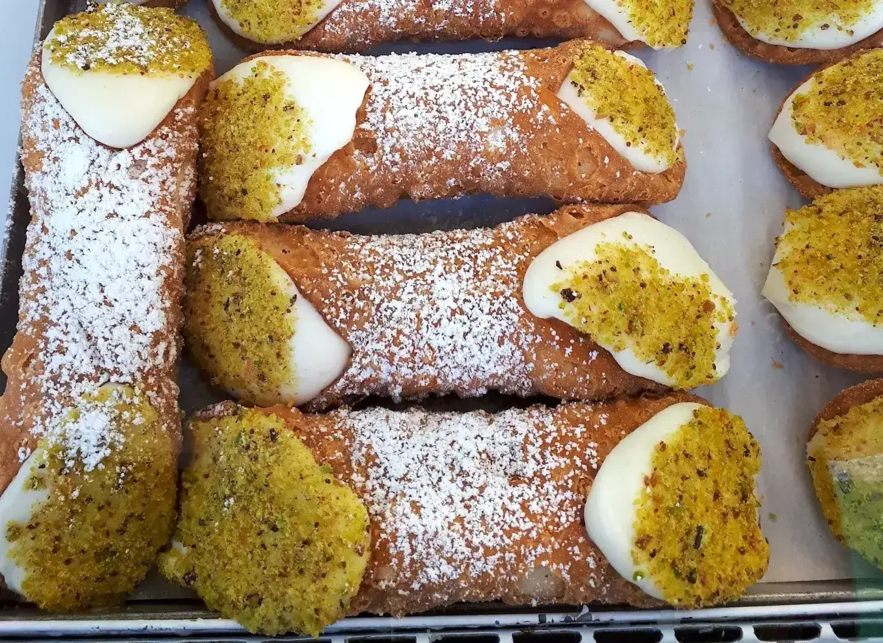 Zbliżenie na sycylijskie cannoli posypane cukrem pudrem i pistacjami, z kremowym nadzieniem.