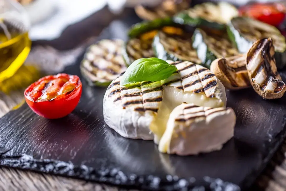Kremowy camembert z grilla z pomidorkiem i warzywami na czarnej desce.