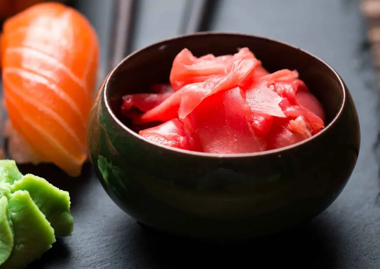 Miseczka z różowym, marynowanym imbirem obok sushi i wasabi. Idealny dodatek do japońskich przysmaków.