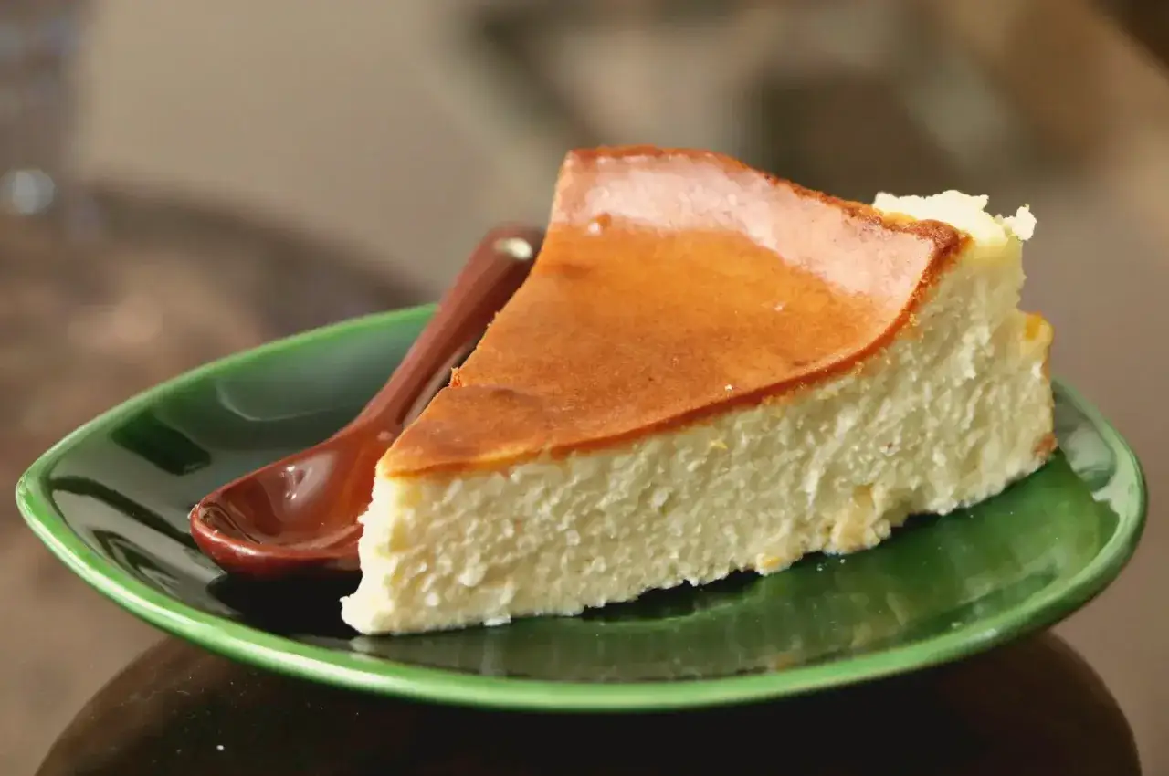 Pyszny kawałek sernika na zielonym talerzyku z łyżeczką. Idealny na deser, choć warto pamiętać o jego sernik kcal.