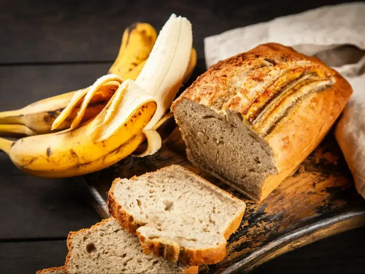 Wilgotne ciasto bananowe, z kawałkami bananów na wierzchu i obok, na drewnianej desce.