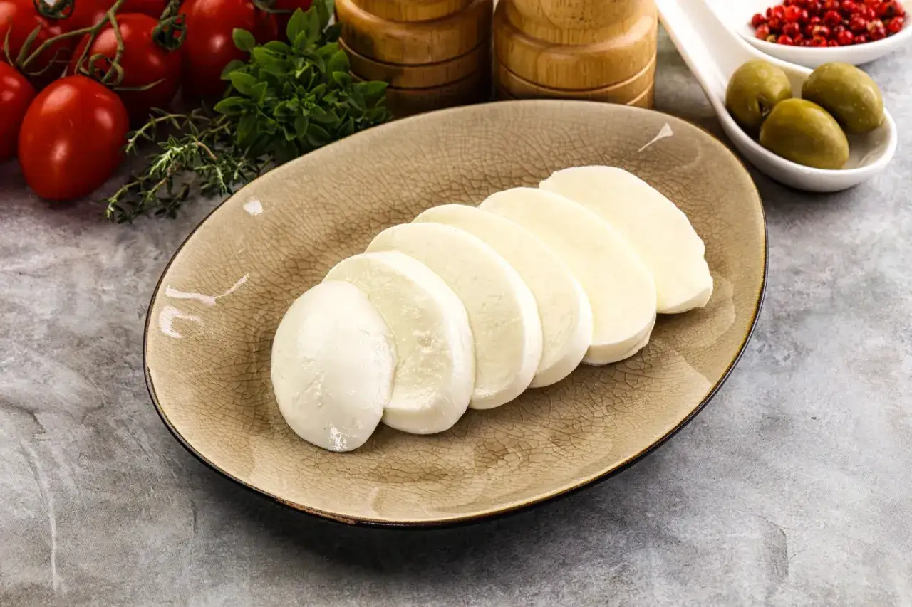 Plasterki mozzarelli na talerzu, obok pomidorki i oliwki. Idealne do sałatki, gdy liczymy mozzarella kcal.