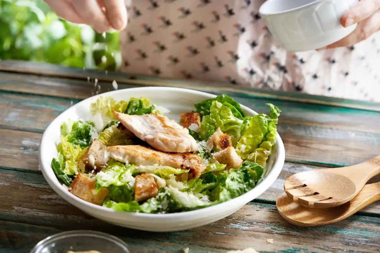 Przygotowanie sałatki cezar z oryginalnym przepisem: świeża sałata, grillowany kurczak, grzanki i parmezan.