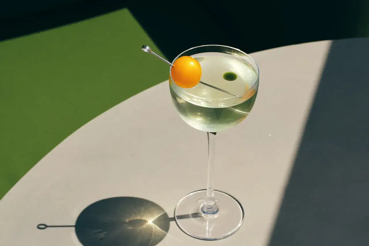 Elegancki kieliszek z drinkiem Martini Bianco, ozdobiony pomarańczową kulką i zieloną kropelką.